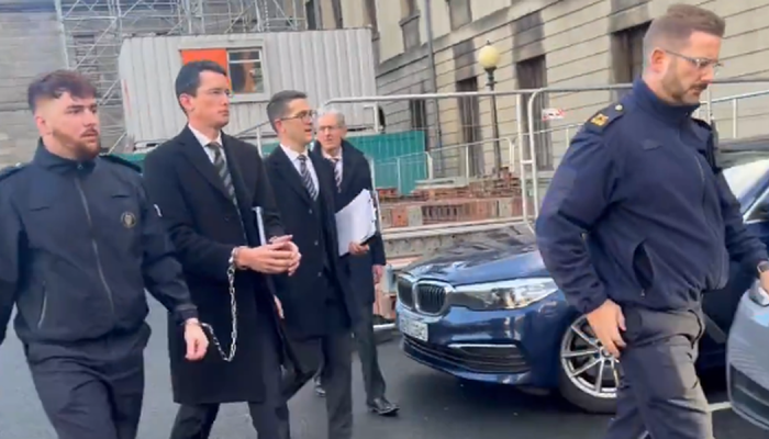 O professor Enoch Burke sendo levado pela polícia com as mãos acorrentadas. (Captura de tela/X/...